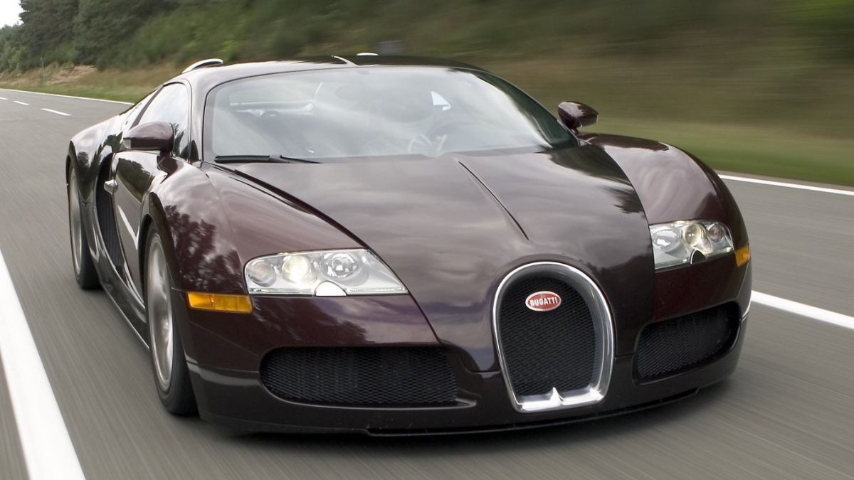 Dark red and black Bugatti Veyron EB 16.4 coupe driving on a tree-lined road