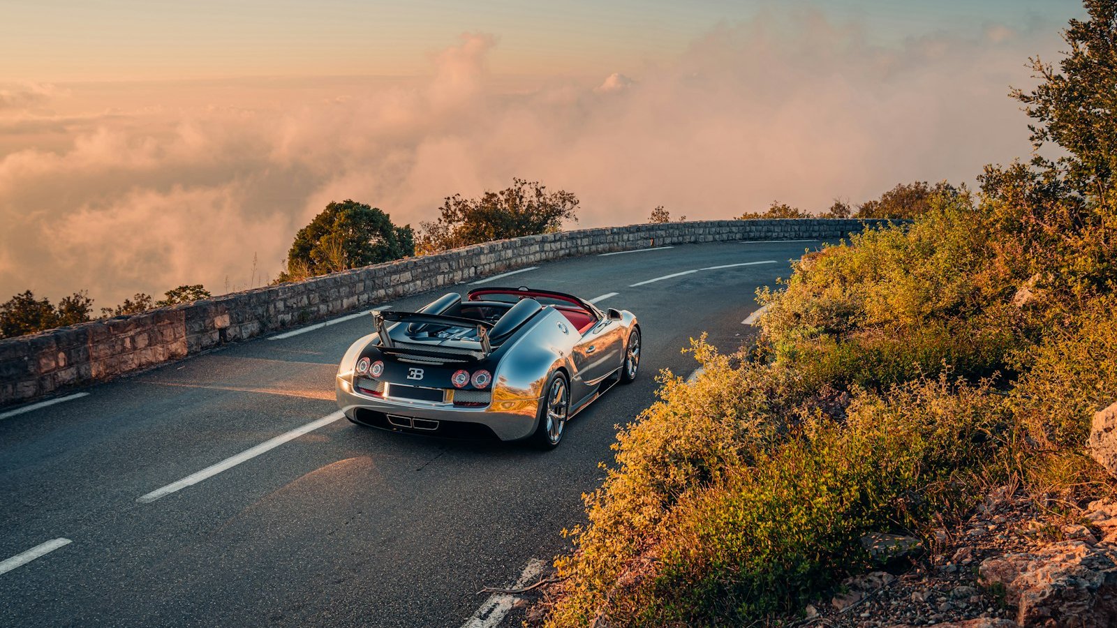 Polished-aluminum Bugatti Veyron Grand Sport Vitesse on a coastal mountain road at sunset