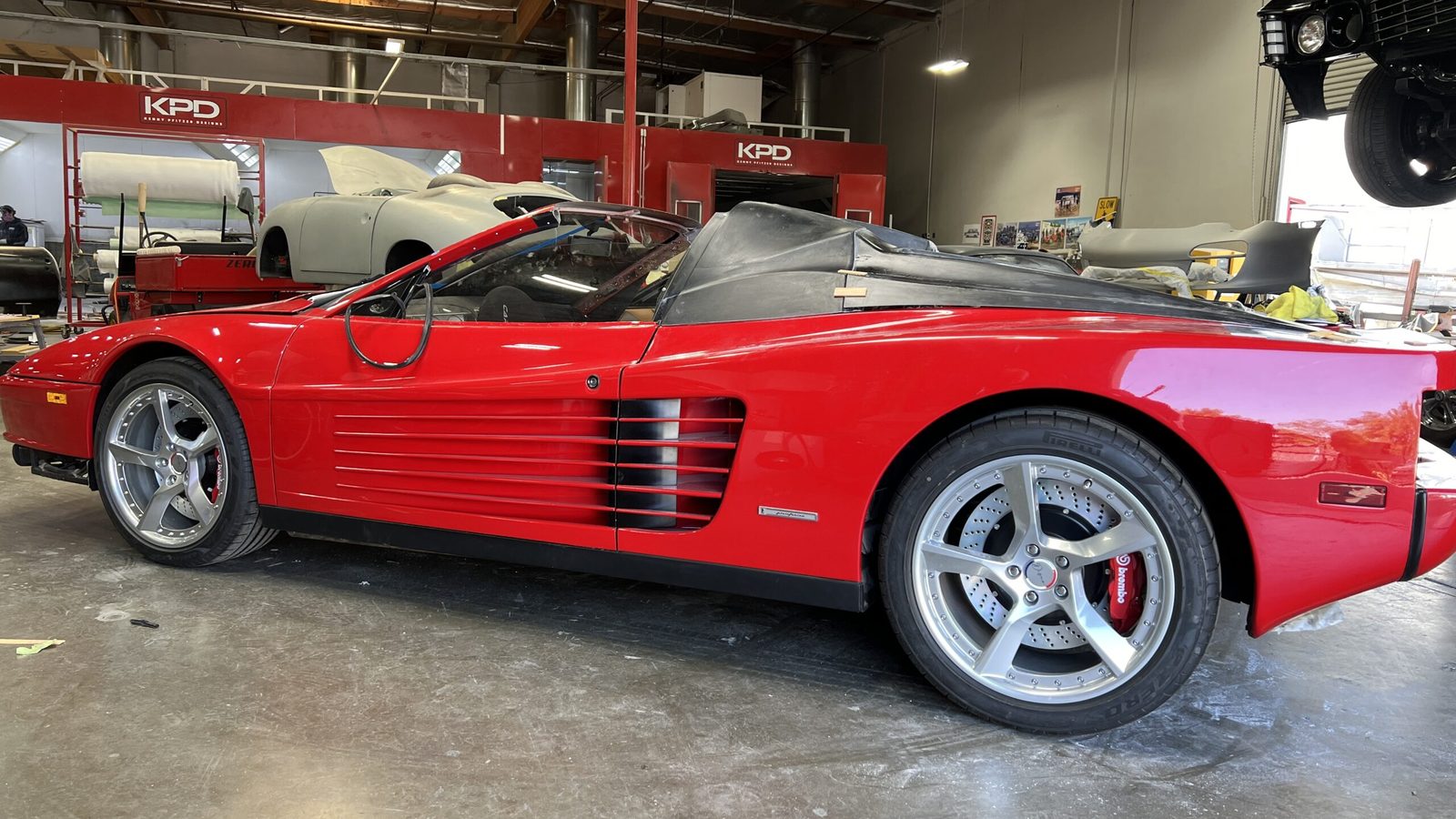 Red Ferrari Testarossa with its roof removed, parked in a workshop during the Tesoro build