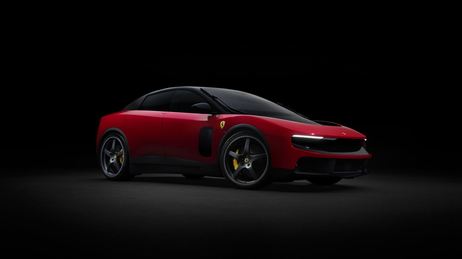 Red Ferrari Luce four-door electric car with black roof, front three-quarter view, lights on, in a dark studio