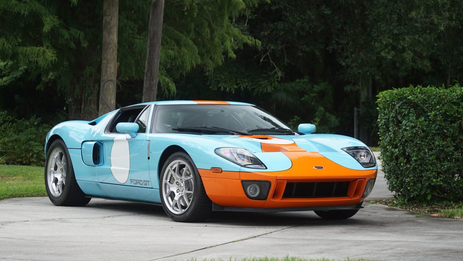 The 554-mile 2006 Ford GT Heritage Edition in Gulf-style light blue and orange, parked on a driveway in front of tropical trees