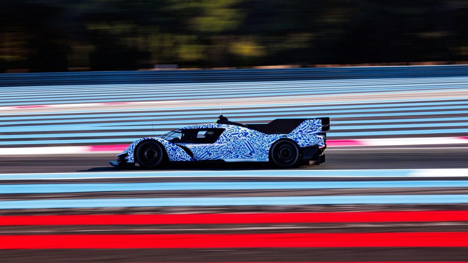 Camouflaged blue-and-white Ford Le Mans Hypercar prototype at speed on the Paul Ricard circuit, side view