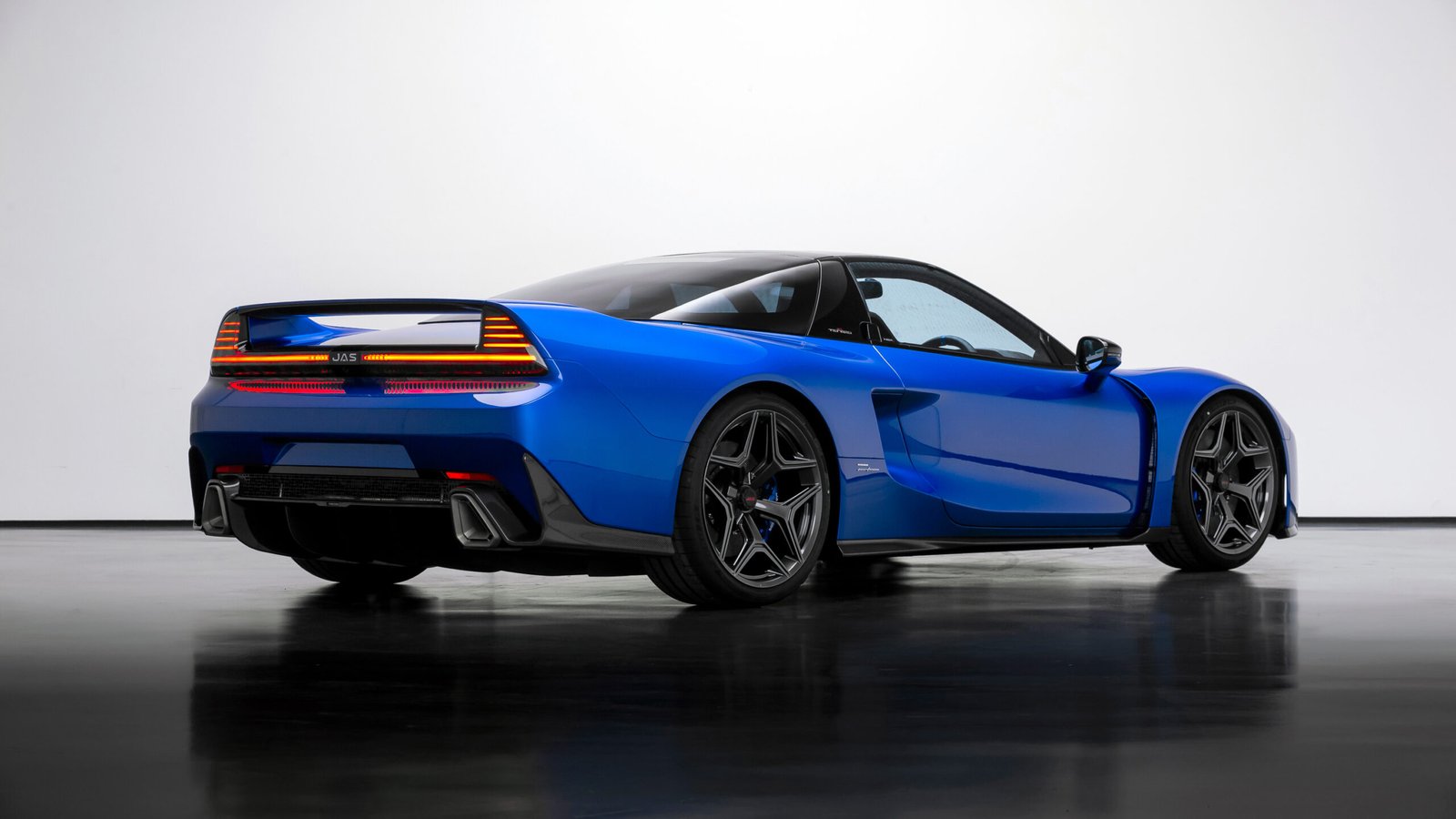 Rear three-quarter view of the blue JAS Tensei showing a full-width light bar, integrated rear wing and wide rear wheel arches in a white studio