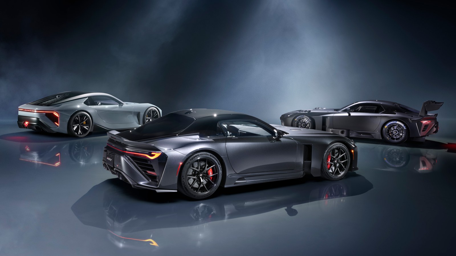 Three low sports cars on a dark reflective studio floor: a silver Lexus LFA Concept at left, a dark gray Toyota GR GT in front and a Toyota GR GT3 race car with a large rear wing at right