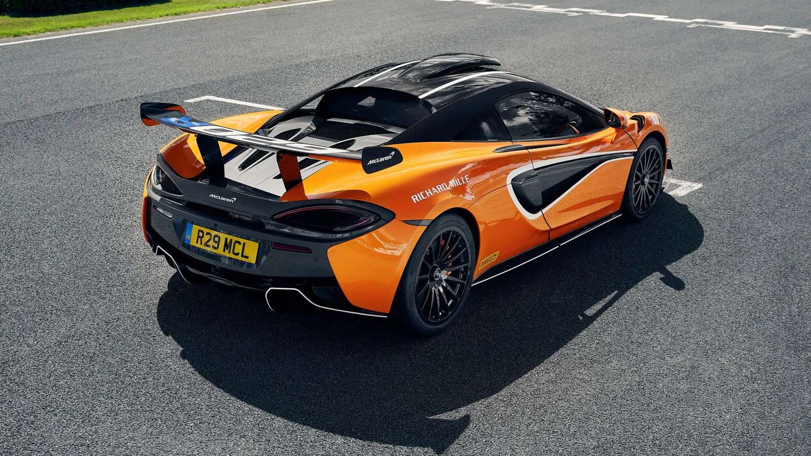 Orange McLaren 620R in Richard Mille livery seen from above and behind on a track, with a roof scoop on the roof and exhaust tips low at the rear bumper