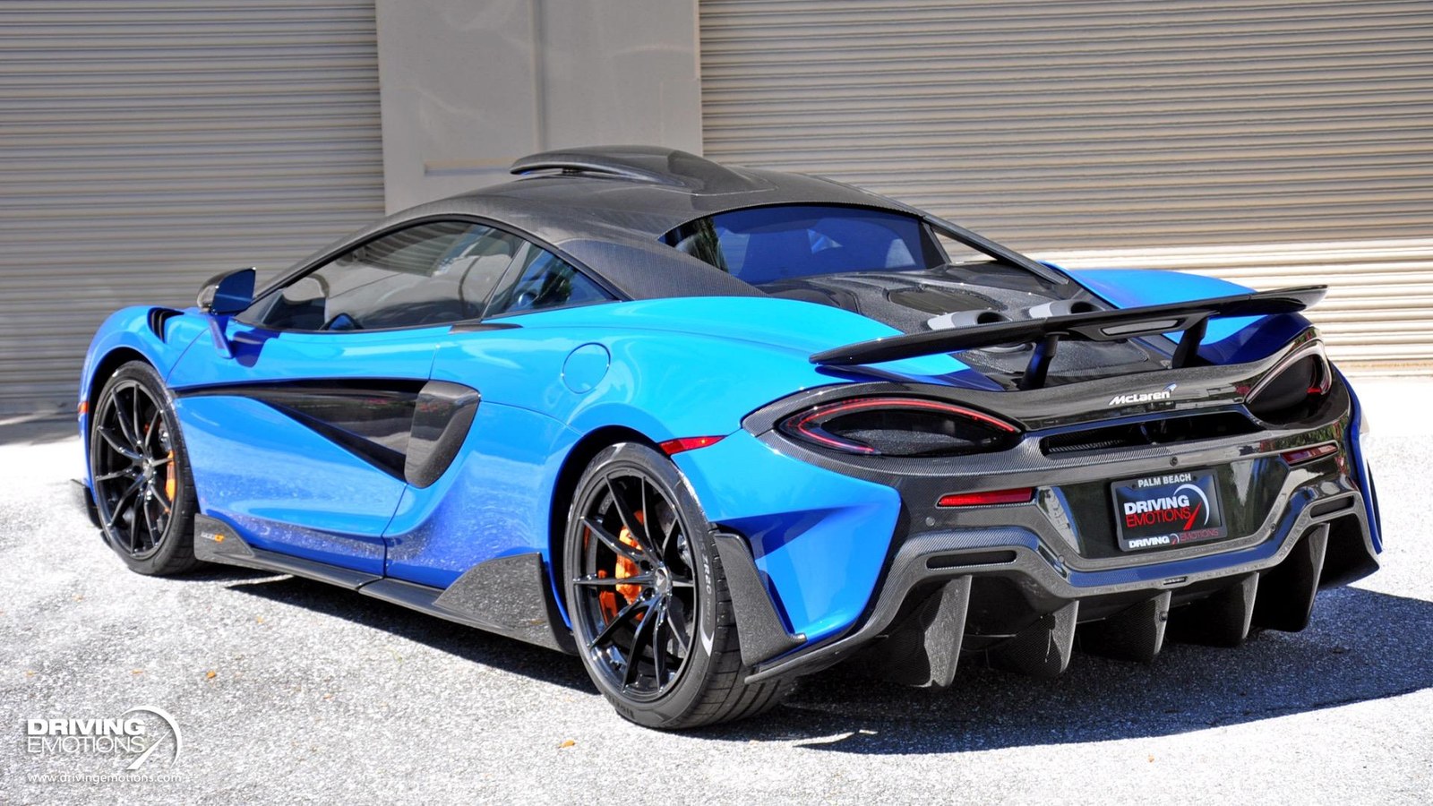 Blue McLaren 600LT coupe from the rear three-quarter, showing the carbon roof scoop on the roof and the top-exit exhaust pipes under the rear wing