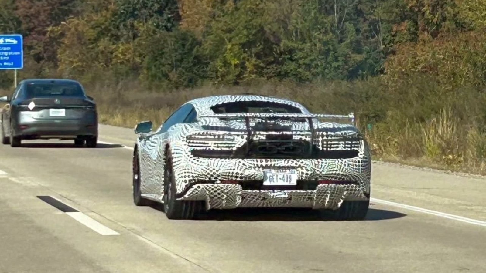 Camouflaged McLaren prototype on a Michigan highway, rear view with fixed wing and twin central exhausts