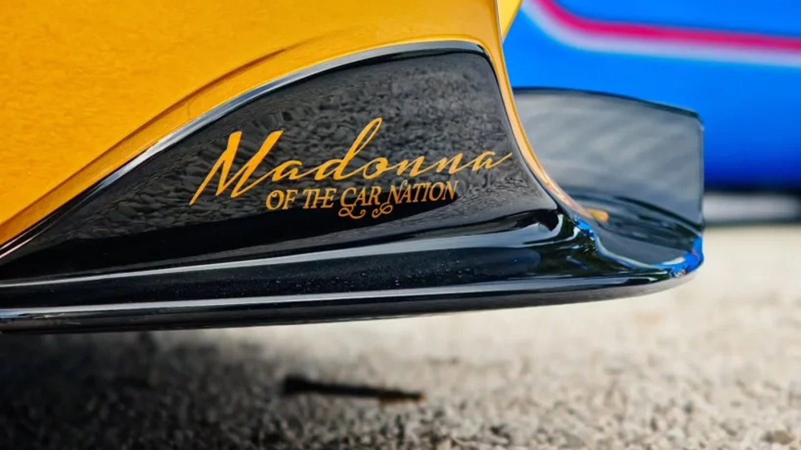 Close-up of the gold Pagani Utopia's black front splitter with 'Madonna of the Car Nation' lettered in gold script