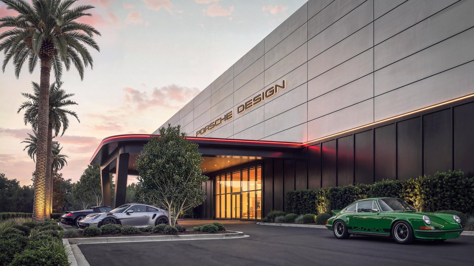 Rendering of the Porsche Design Concours West Palm Beach entrance at dusk: a pale paneled facade with illuminated PORSCHE DESIGN lettering, a canopy edged in a red light strip over a glass entrance, palm trees, and a green classic 911 Carrera RS 2.7, a silver 911 GT3 RS and a Carrera GT parked out front