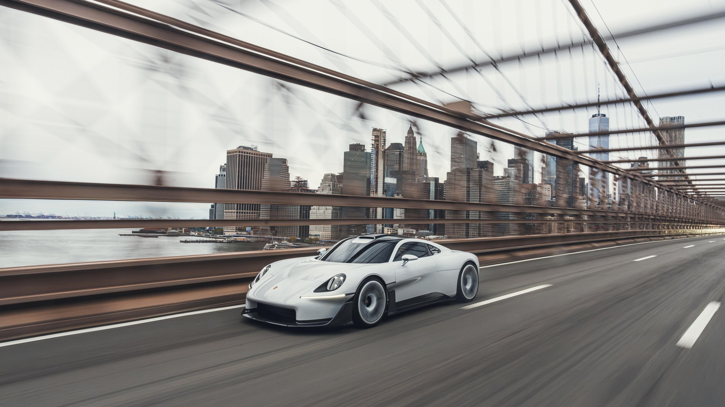 A white Porsche Mission S vision model driving across the Brooklyn Bridge, with the Lower Manhattan skyline and the East River behind it