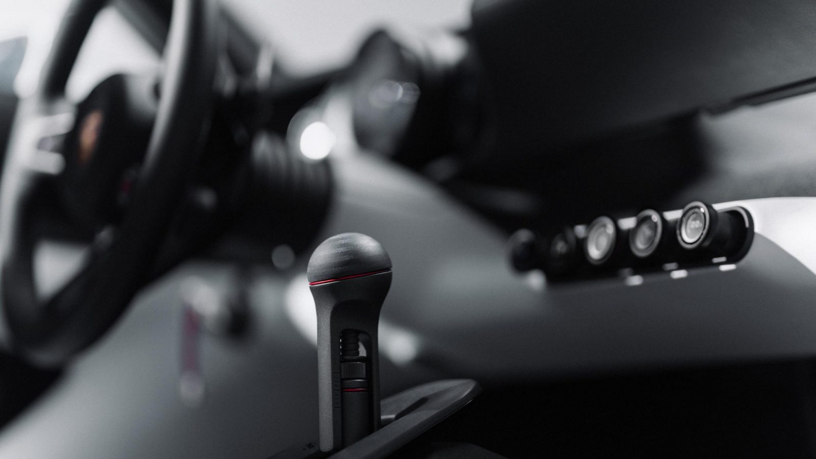 Close-up of the Mission S console with a tall black gear lever topped in red and a row of round toggle controls on the dash beyond it, with the steering wheel blurred in the foreground