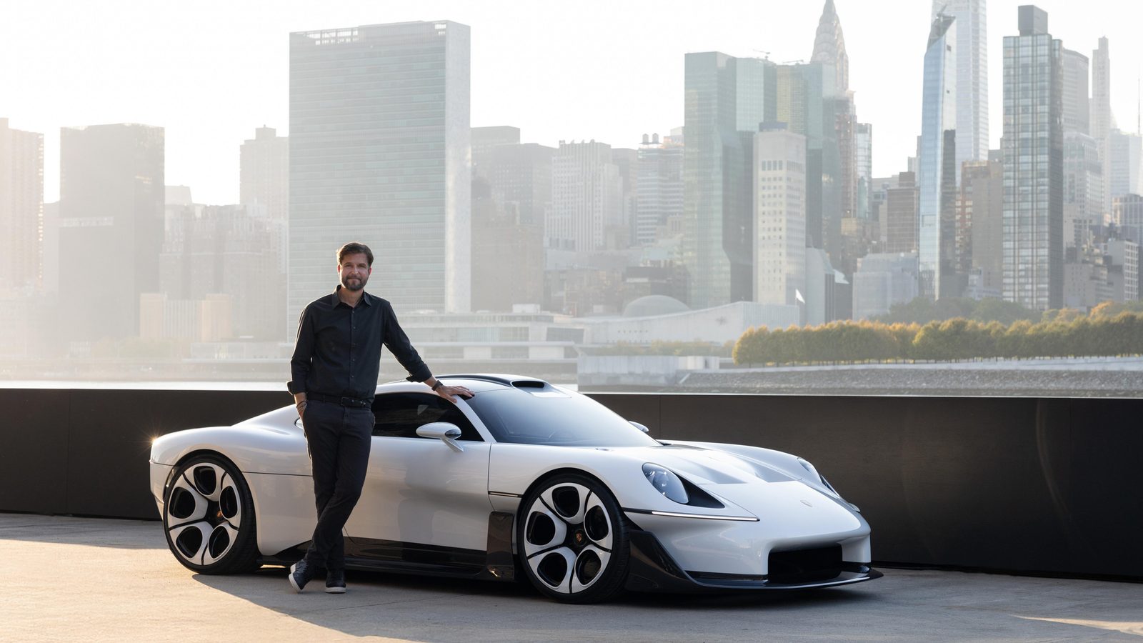 Tobias Sühlmann, Porsche's Head of Style, leaning on the white Mission S on a waterfront pier with the Manhattan skyline, including the United Nations building, behind