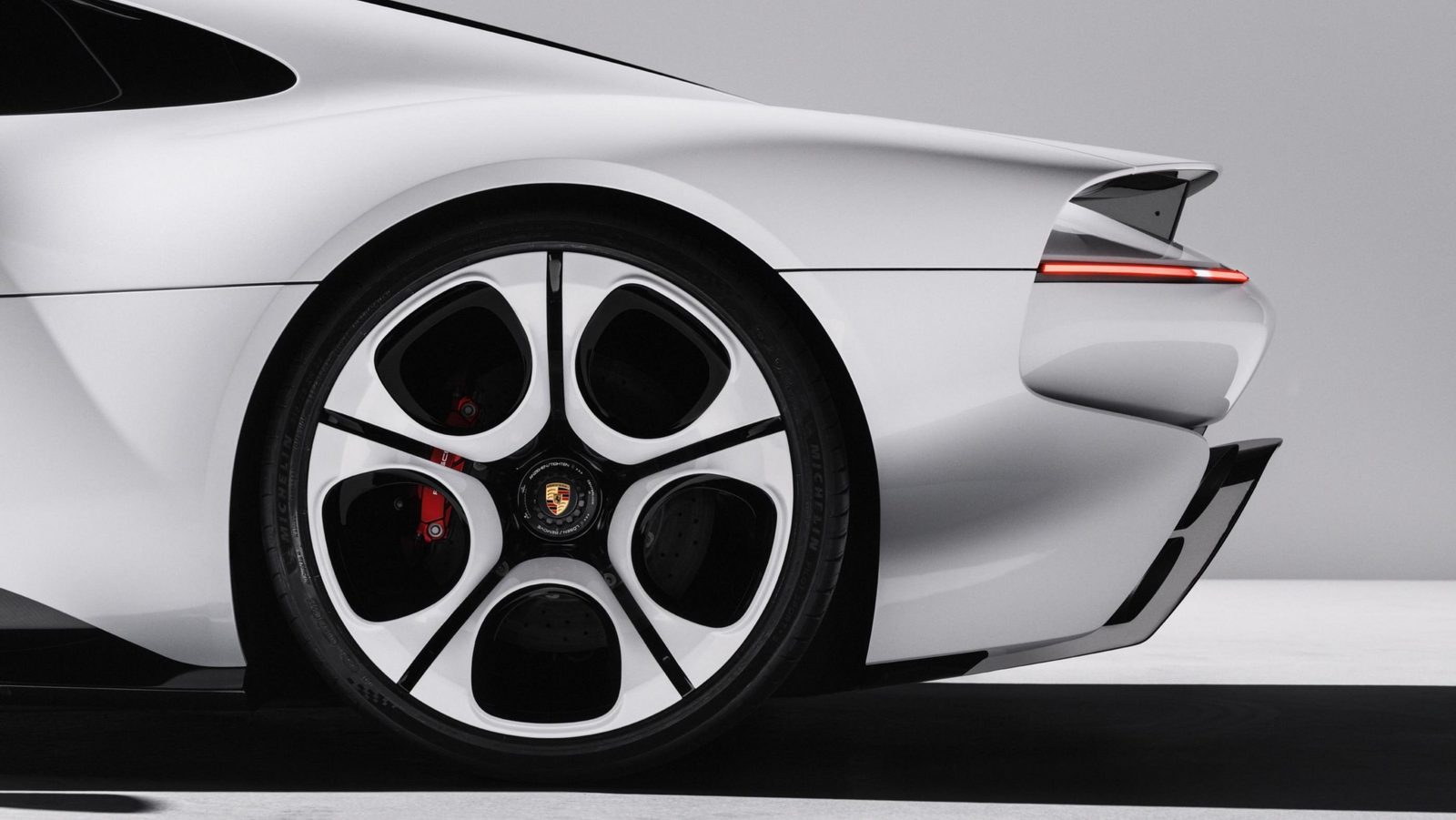 Close-up of the Mission S rear wheel, a white five-spoke design with black openings and a Porsche crest center, with a red brake caliper and a thin red light strip on the rear deck above